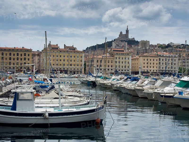 Harbour with many boats, behind it colourful buildings and a hill with a church, Marseille at the mediterranean sea with the old cathedral and ships in the historic harbour, rocky coast at the mediterranean sea, marseille, france