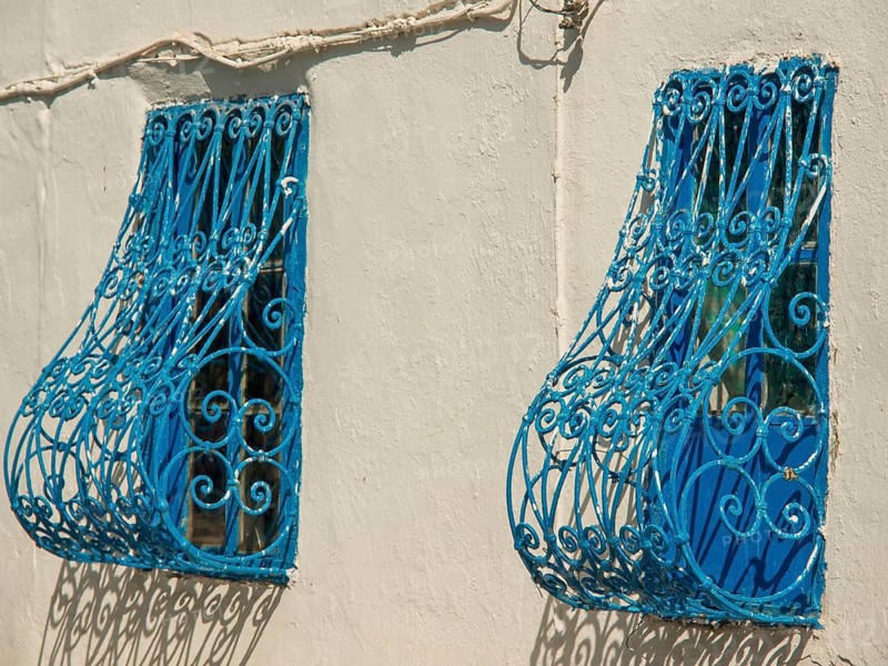 Two windows with decorative blue metal grilles on a light-coloured wall, Tunis in Africa with ruins from Roman times, modern mosques and blue and white houses in sidi-bou-said, Tunis, Tunisia, Africa