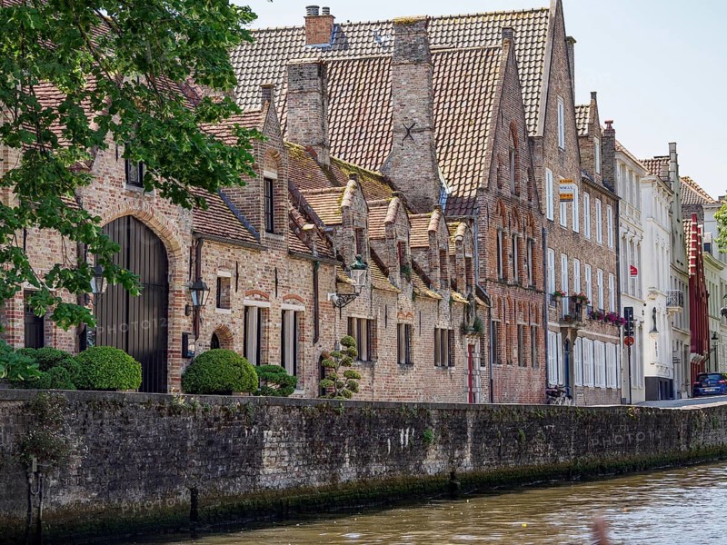 Historic buildings on the canal with decorative gables and green trees, historic city on the river with ornate gables, old facades and historic towers, Bruges, Belgium, Europe