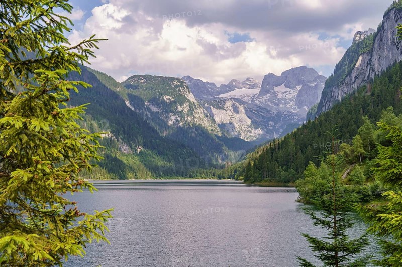 Spectacular lake surrounded by steep mountains and dense forest under a cloudy sky, turquoise green mountain lake with high mountains and green trees in the background, gosau, austria