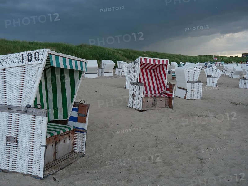 Many beach chairs stand on the sandy beach under an oppressively cloudy sky near the dunes, the north sea island baltrum with grassy dune, colourful beach chairs on the beach and clouds over the sea, Baltrum Germany