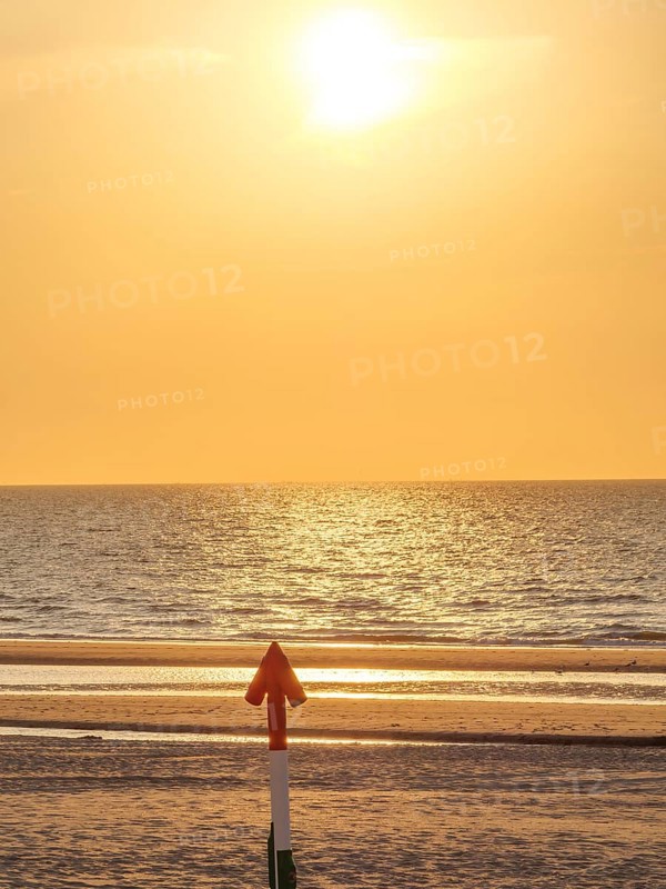 An arrow on the beach points towards the sea at sunset, the sky shines in golden light, sunset on the beach at de haan on the north sea, de han, belgium
