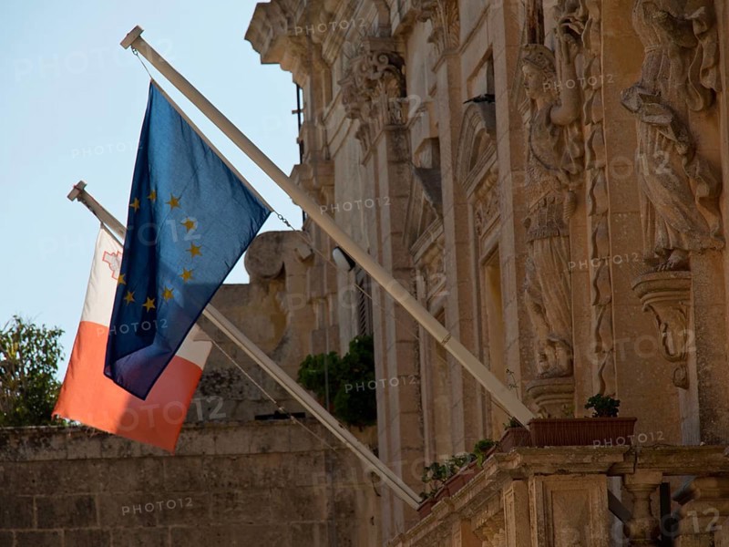 Two flags, one of the EU and one of Malta, in front of historic stone architecture, the town of mdina on the island of malta with historic houses, colourful balconies, magnificent churches, mdina, Malta, Europe