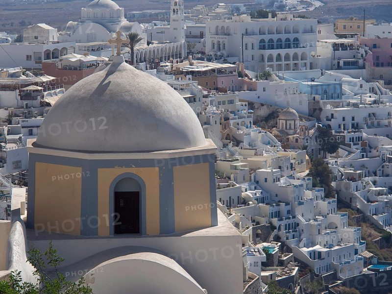 Elevation overlooking a town of white buildings and a large dome, typical of Mediterranean towns, The volcanic island of Santorini with blue and white houses and churches, flowers and palm trees on a volcanic island, santorini, greece
