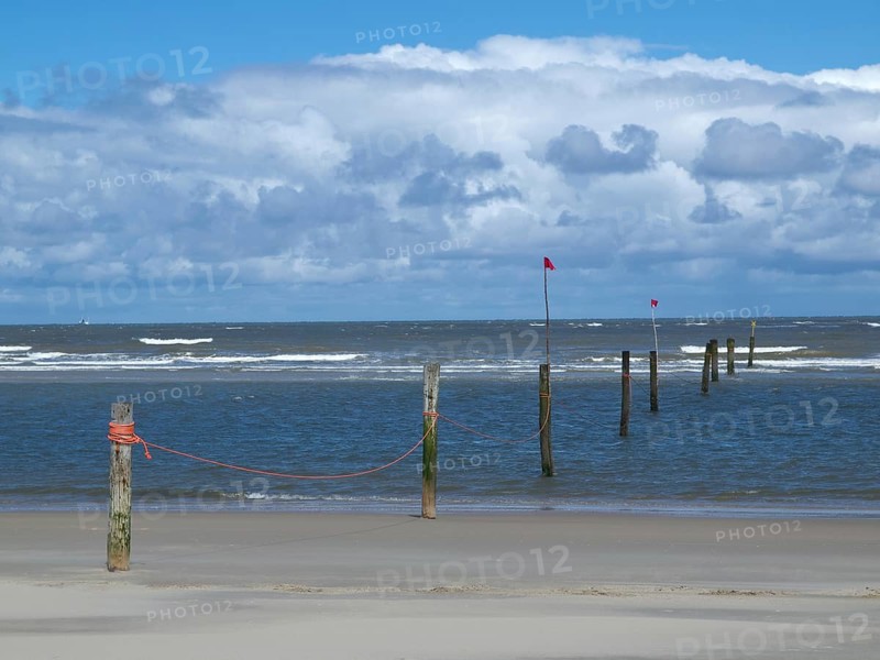 Sandy beach beach with poles and red flags in the water, cloudy sky, view of the wide sea with clouds in the sky, Norderney, Germany, Europe