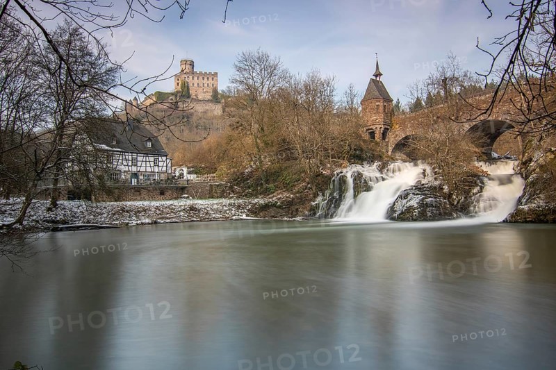Beautiful landscape in winter with ice and snow. Waterfall of the river Elz near the castle Pyrmont, the country inn Pyrmonter Muehle directly at a lake. A historic bridge in Rhineland-Palatinate, Germany, Europe