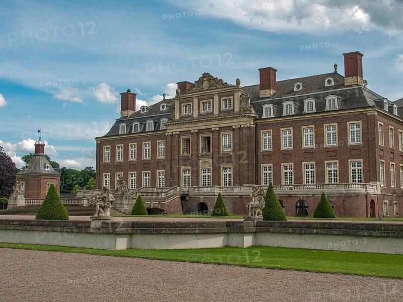 Historic castle with manicured lawn and sculptures, surrounded by a stone wall under a cloudy sky, historic castle with a green park with sculptures and paths, nordkirchen, germany
