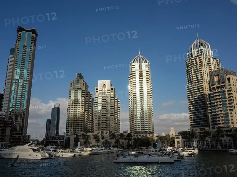 Boats in a marina in front of a row of modern skyscrapers under a cloudless sky, Dubai, Arab Emirates