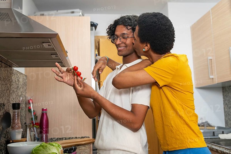 Tender gay couple in love kissing while preparing salad at home