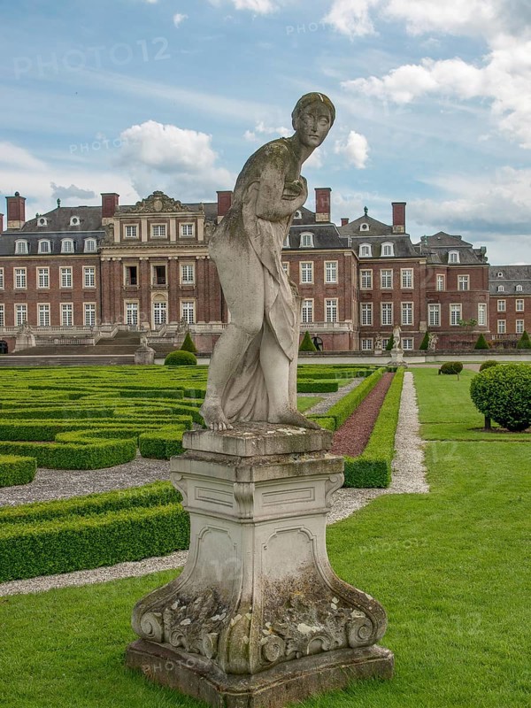Sculpture in a well-kept garden with a baroque castle in the background, blue sky with clouds, historic castle with a green park with sculptures and paths, nordkirchen, germany