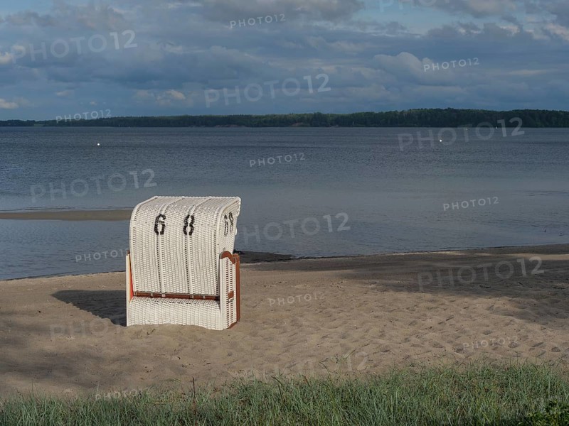 Single white beach chair on deserted sandy beach, with cloudy sky and calm sea, colourful beach chairs on a small sandy beach on the Baltic Sea, Eckernfoerde, Germany, Europe