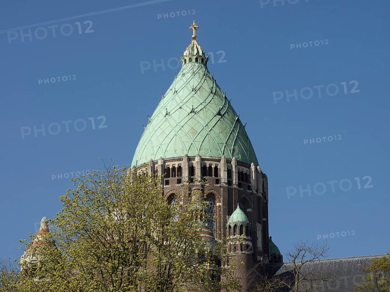 The upper part of a church tower with a greenish dome and a golden cross surrounded by tree tops, Haarlem, Netherlands