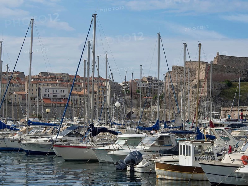 A marina full of boats with buildings and a hill behind it, Marseille on the Mediterranean Sea with the old cathedral and ships in the historic harbour, rocky coast on the mediterranean sea, marseille, france