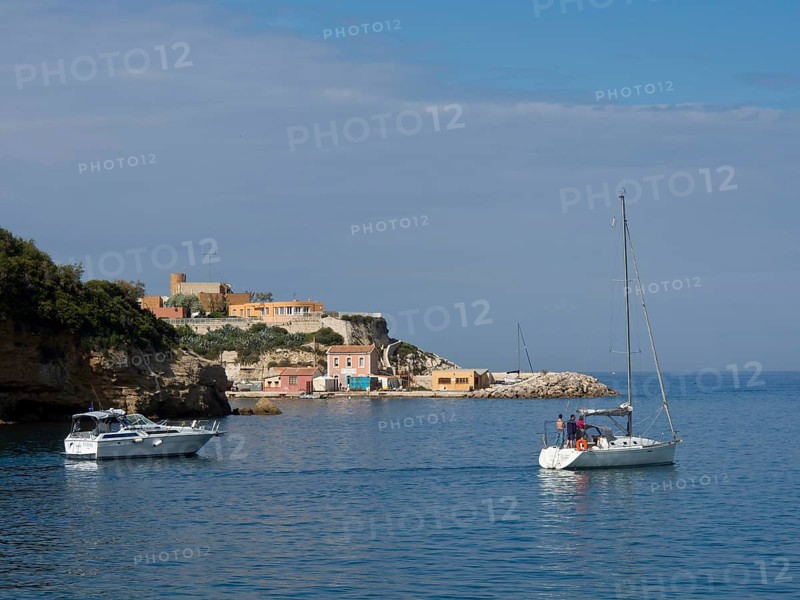Sailing boats in front of a coastal landscape with cliffs and small houses under a partly cloudy sky, Marseille on the Mediterranean Sea with the old cathedral and ships in the historic harbour, rocky coast on the Mediterranean Sea, marseille, france