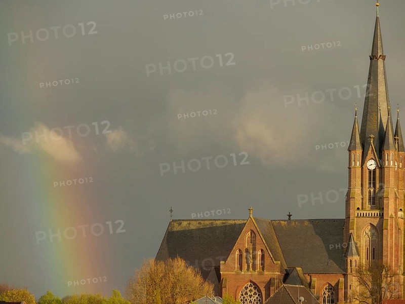 A gothic church with a high tower under a cloudy sky and a rainbow in the background, rainbow at a church in Muensterland, Borken, Germany, Europe
