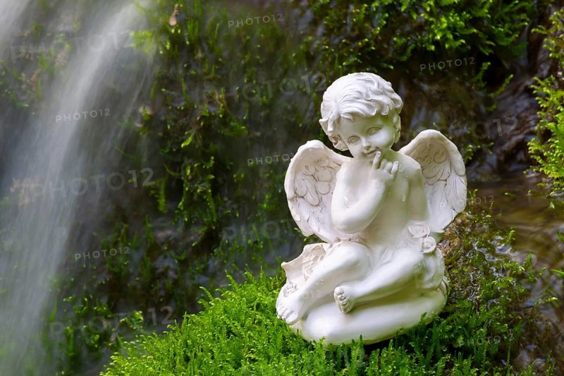 Porcelain angel figurine on moss by a waterfall