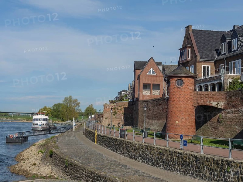 Historic brick buildings along a riverside footpath in sunny weather with a slightly cloudy sky, the rhine promenade of Rees with flowers and trees, rees, germany