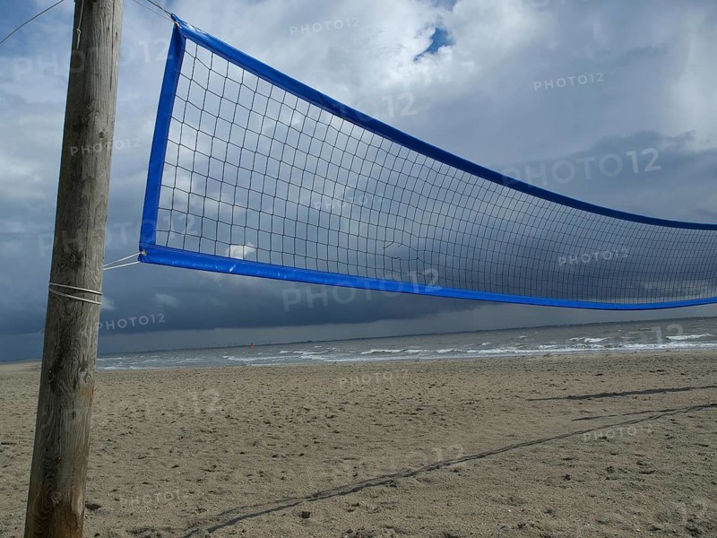 A volleyball net on the beach under a cloudy sky and slightly stormy weather with the sea in the background, blue beach volleyball net on a beach with white clouds, norderney, germany