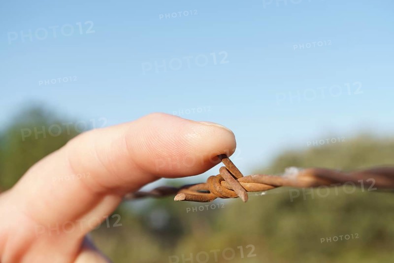 Close-up of a woman's finger stabbing herself with rusty barbed wire