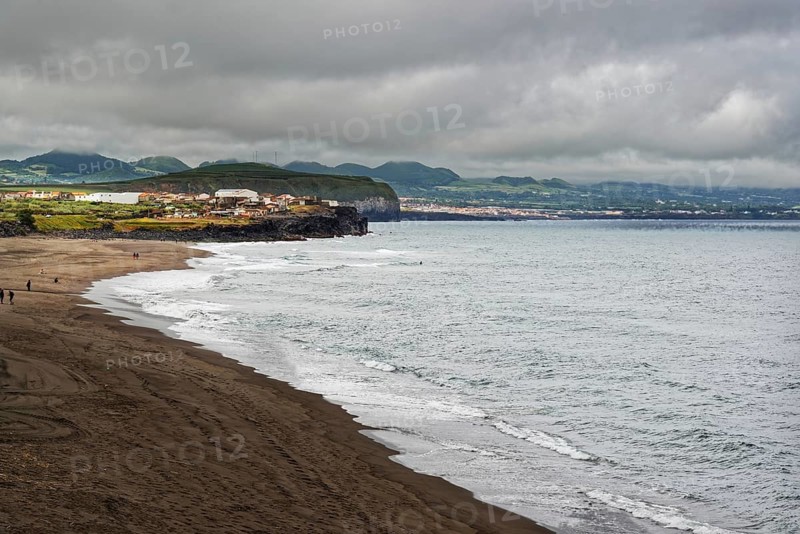 A vast coastline with a sandy beach and gentle waves, surrounded by cloudy skies and distant hills, coastal town of Ribeira Grande, Santa Barbara, Sao Miguel, Azores, Portugal, Europe