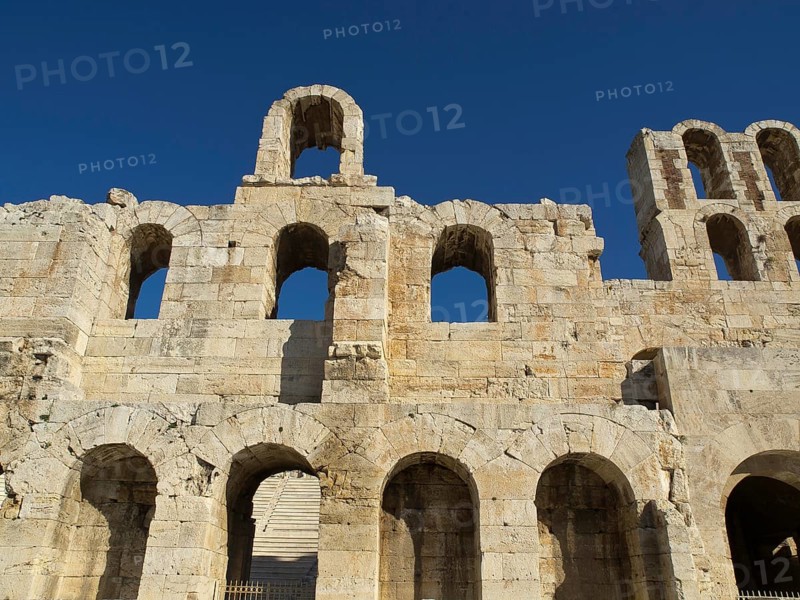 Ancient stone structure with multiple arches under a clear blue sky, Ancient buildings with columns and trees on the Acropolis in Athens against a blue sky, athens, greece