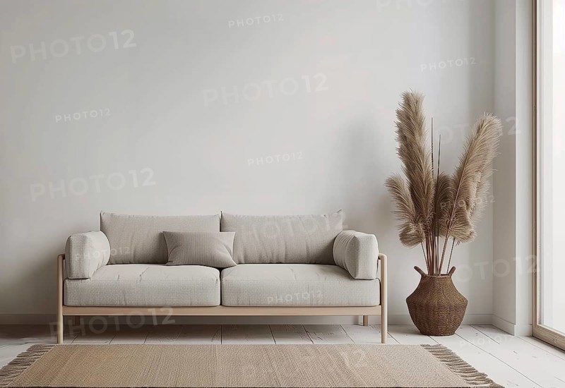 A couch sits in front of a white wall. Potted feather grass sit on the floor next to the couch. The room is empty and has a minimalist feel, AI generated