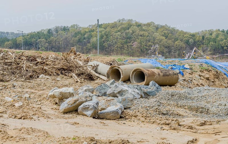 Old dirty concrete culvert sections on ground beside tree branches at construction site in Daejeon, South Korea, Asia