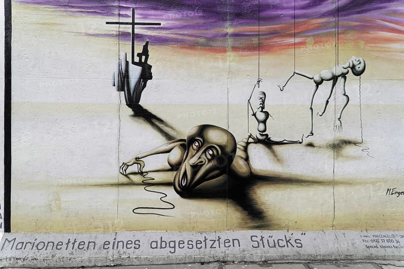 Marc Engel, Painting marionettes of a detached piece by Marc Engel on a remnant of the Berlin Wall, East Side Gallery, Graffiti on the Berlin Wall in the East Side Gallery, Berlin, Germany, Europe, Surreal scene with melancholic figures and a large cross in front of a gloomy background, Warschauer Strasse, Europe