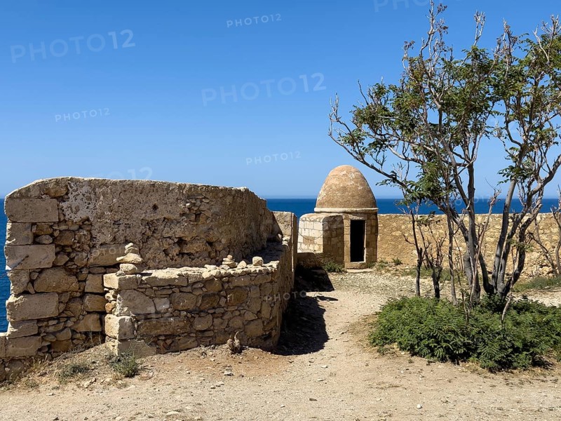 Left wall with crenellated gap for guns behind one of 10 ten round watchtowers of historic fortress Fortetza Fortezza of Rethymno built by Republic of Venice in 16th century in northwest of old town of Rethymno on rocky hill Paleokastro on north coast of island Crete, in background Aegean Sea Aegean Cretan Sea Mediterranean, Rethymno, Crete, Greece, Europe