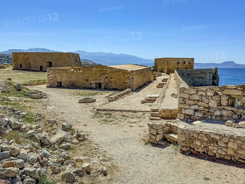 View of partly preserved old buildings on plateau of fortress, left rear former house of governor of Venice centre front warehouse right rear house of aldermen, in front right fortification wall of historic fortress Fortetza Fortezza of Rethymno built by Republic of Venice in 16th century in northwest of old town of Rethymno on rocky hill Paleokastro on north coast of island Crete, in background Aegean Sea Aegean Cretan Sea Mediterranean, Rethymno, Crete, Greece, Europe