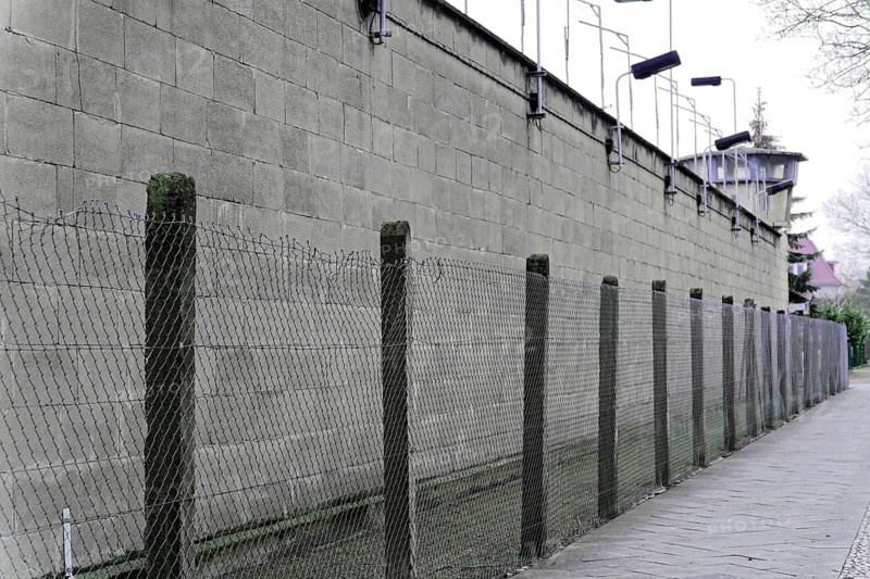 High concrete wall with wire mesh fence and security lighting. Gloomy, cold atmosphere, Berlin-Hohenschoenhausen Memorial, former headquarters, Stasi remand centre, Berlin, Germany, Europe
