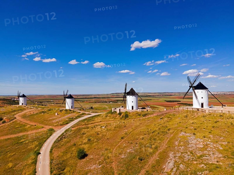 Four windmills stand on a hill under a bright blue sky in a vast summer landscape, aerial view, Alcazar de San Juan, Ciudad Real, Castilla-La Mancha, Spain, Europe