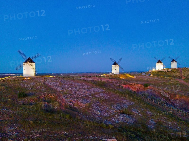 Several windmills on a hill at dusk in a wide field landscape under a clear sky, aerial view, Alcazar de San Juan, Ciudad Real, Castilla-La Mancha, Spain, Europe