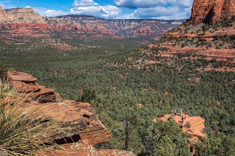 Hikers climb to the top of a red rock sandstone formation along the Devil's Bridge Trail in Sedona, Arizona, USA, North America