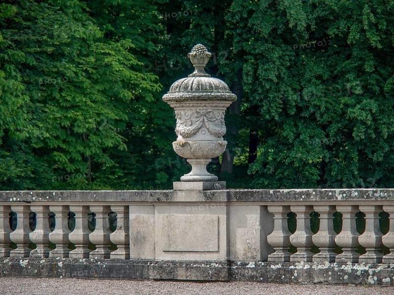 Stone sculpture in a well-kept garden, surrounded by a balustrade and green foliage in the background, old red brick castle with towers and a large park with trees, plants and statues, Nordkirchen, Germany, Europe
