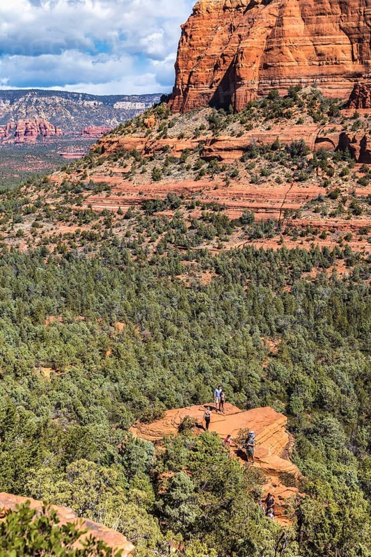 Hikers climb to the top of a red rock sandstone formation along the Devil's Bridge Trail in Sedona, Arizona, USA, North America