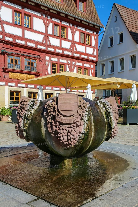 Fountain with inscription Gemmingen, stone grapes, water features, Ratsstueble restaurant at the back, traditionally a restaurant, pub, half-timbered house, three-storey half-timbered building with solid ground floor, gabled roof, ornamental half-timbering, bay windows, sunshades, Boennigheim, Ludwigsburg district, Baden-Wuerttemberg, Germany, Europe