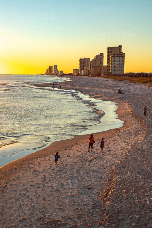 People walking and playing on the beach as the sun sets over the Gulf of Mexico at Gulf Shores, Alabama, United States of America, USA, North America