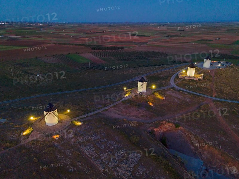 Night shot of several illuminated windmills on hills in a wide field landscape at dusk, aerial view, Alcazar de San Juan, Ciudad Real, Castilla-La Mancha, Spain, Europe