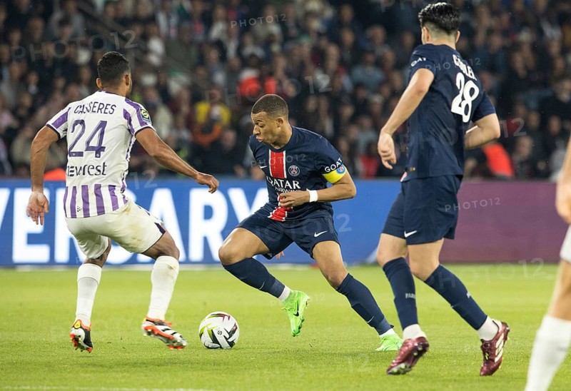 Football match, captain Kylian MBAPPE' Paris St. Germain right on the ball, Cristian CASSERES Jr. FC Toulouse tries to interfere with him, Carlos SOLER Paris St. Germain seen from behind watching the scene, Parc des Princes football stadium, Paris, France, Europe