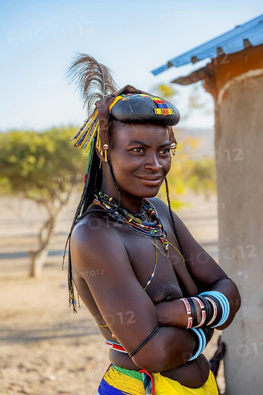 Hakaona woman with traditional kapapo hairstyle and hair ornaments with ostrich feathers and colourful necklaces, portrait, in the morning light, Angolan tribe of the Hakaona, near Opuwo, Kunene, Namibia, Africa