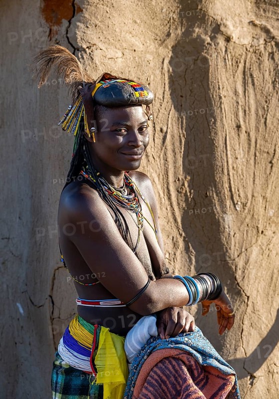 Hakaona woman with traditional kapapo hairstyle and hair ornaments with ostrich feathers and colourful necklaces, portrait. in the morning light, Angolan tribe of the Hakaona, near Opuwo, Kunene, Namibia, Africa