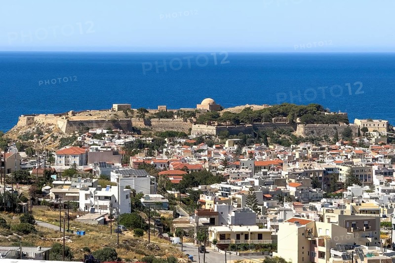 View from elevated position over rooftops of city of Rethymno on fortress walls and ruins of historic fortress Fortetza Fortezza of Rethymno built by Republic of Venice in 16th century in northwest of old town of Rethymno on hill Paleokastro on north coast of island Crete, behind Aegean Cretan Sea Aegean Mediterranean, Rethymno, Crete, Greece, Europe