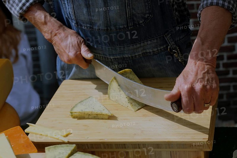 A man in traditional clothing cuts cheese into slices for tasting at the Alkmaar cheese market., Alkmaar, The Netherlands, Europe