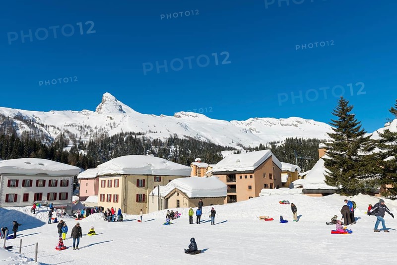 Beautiful Swiss Ski Slope with Houses on the Mountain with Snow in Winter in a Sunny Day with Blue Clear Sky in San Bernardino, Grisons, Switzerland, Europe