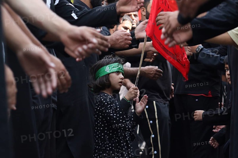 Child holding a red flag among people dressed in black, participating in a solemn procession, Jammu and Kashmir, India, Asia