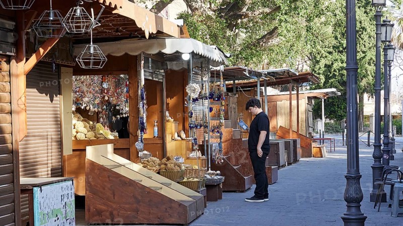 Souvenir shops, Footpath to the Grand Master's Palace, A lively market with various stalls along a street with trees, Young man, Old Town of Rhodes, Rhodes Town, Rhodes, Dodecanese, Greek Islands, Greece, Europe