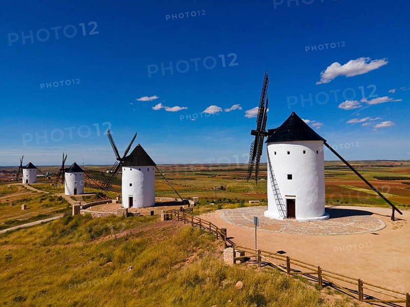 Grouped windmills on a hill under a bright blue sky in a vast summer landscape, aerial view, Alcazar de San Juan, Ciudad Real, Castilla-La Mancha, Spain, Europe