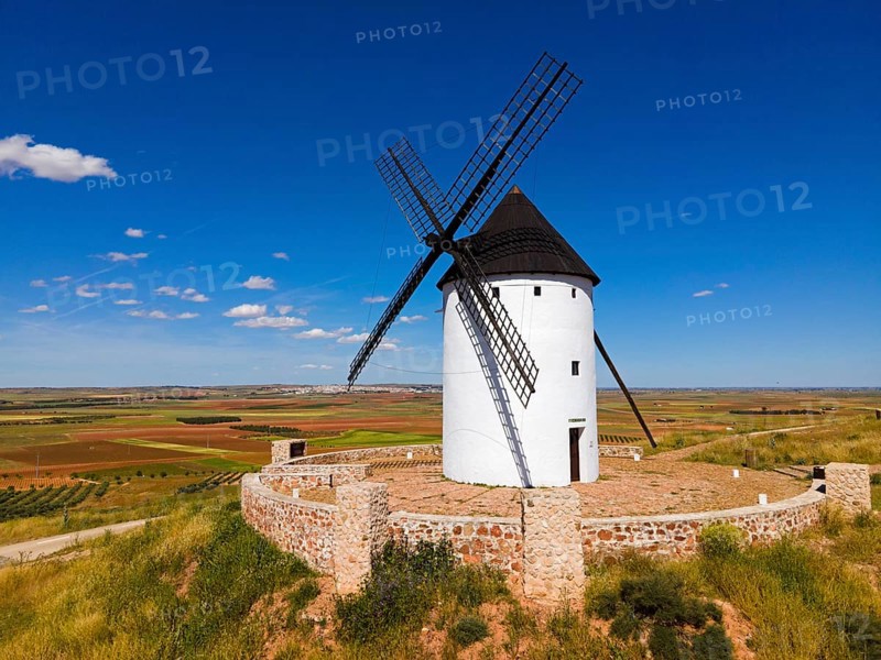 A single windmill on a hill under a bright blue sky in a vast summer landscape, aerial view, Alcazar de San Juan, Ciudad Real, Castilla-La Mancha, Spain, Europe