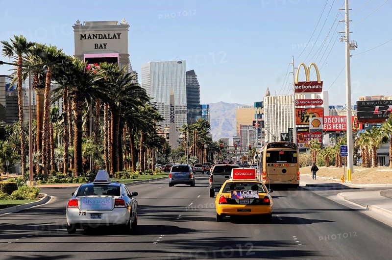 Las Vegas, Nevada, USA, North America, A street with cars and the Mandalay Bay Hotel and various adverts and palm trees, Las Vegas Strip, North America